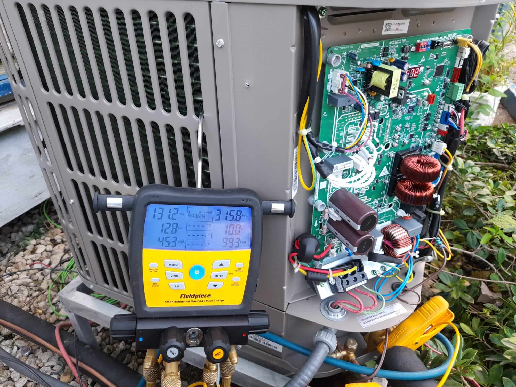Refrigerant gauge manifold connected to an outdoor air conditioning condenser with its control board exposed